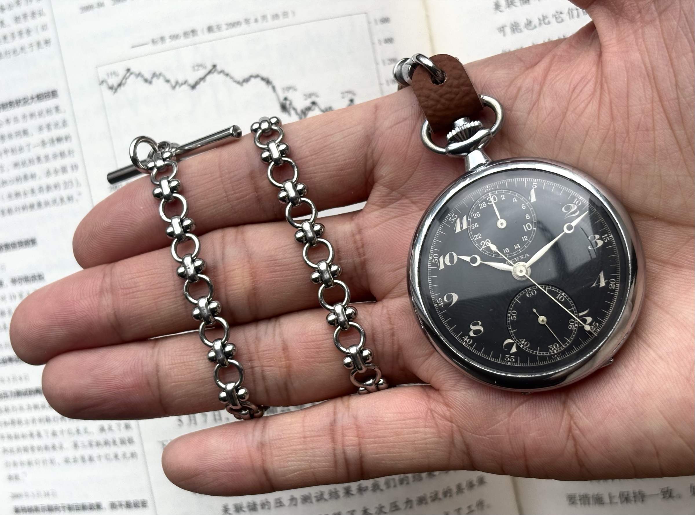 Berna pocket watch and chain resting across a hand over a printed chart