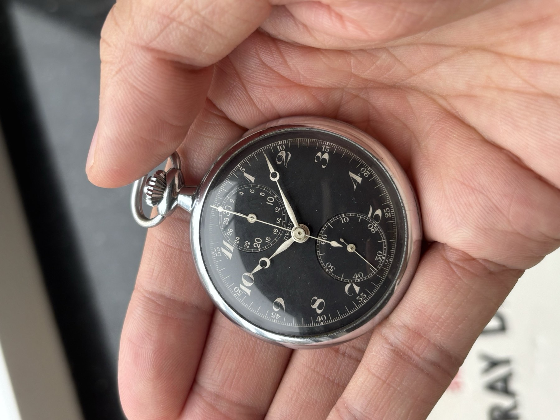 Close view of the Berna pocket watch crown and black dial held in the hand