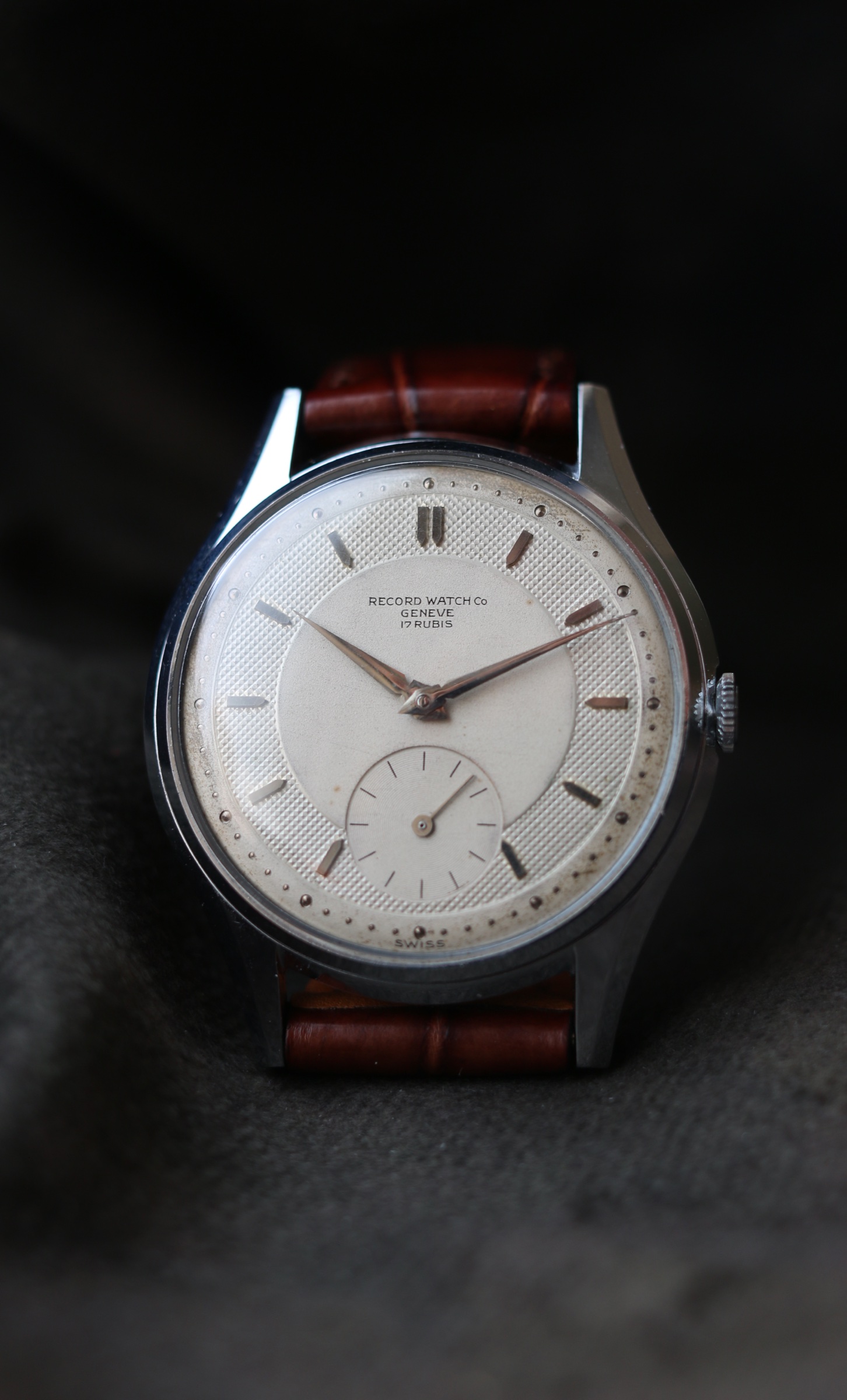 Record Genève wristwatch photographed straight-on against dark fabric